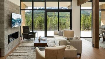 Una sala de estar moderna con chimenea, asientos cómodos, un televisor grande y vistas a un paisaje montañoso.