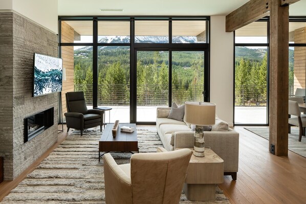 A modern living room with a fireplace, comfortable seating, a large TV, and a view of a mountainous landscape.