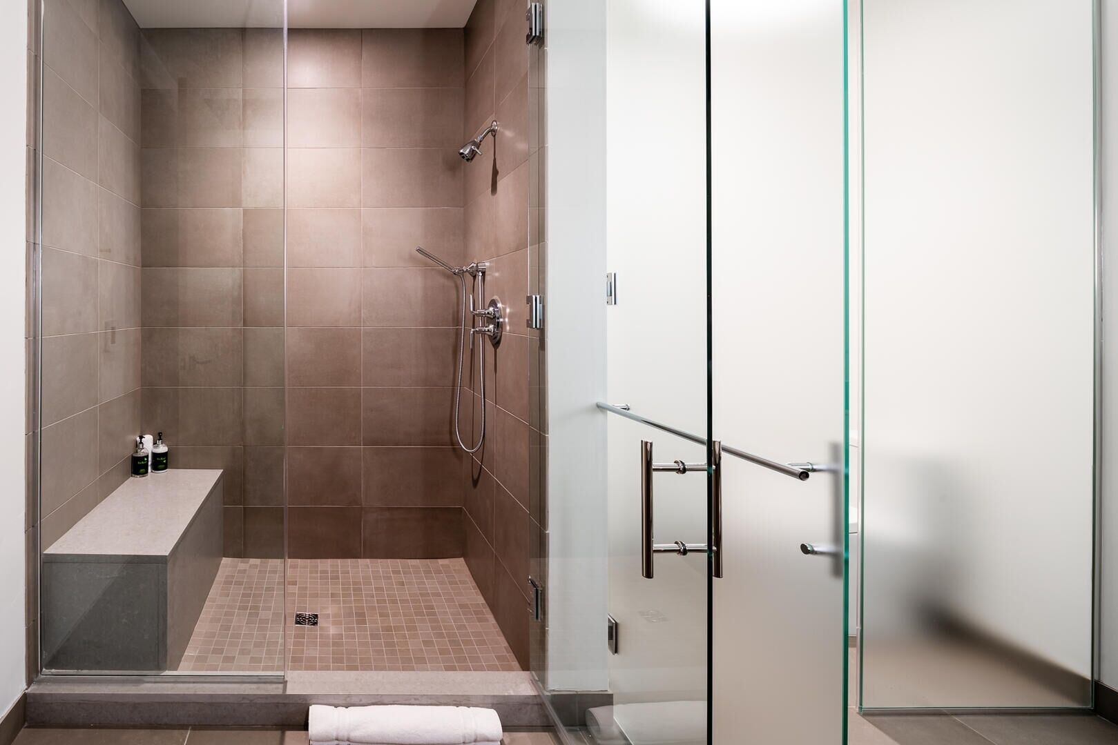 A modern shower area with a glass partition, a bench, and a towel rack.