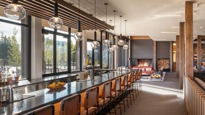 Un área de bar moderna con una barra larga, varios taburetes y amplias ventanas que ofrecen vistas al exterior.