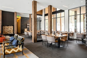 Un espace de repas moderne avec de grandes poutres en bois apparentes, de grandes fenêtres et un mur en pierre agrémenté d’une cheminée.