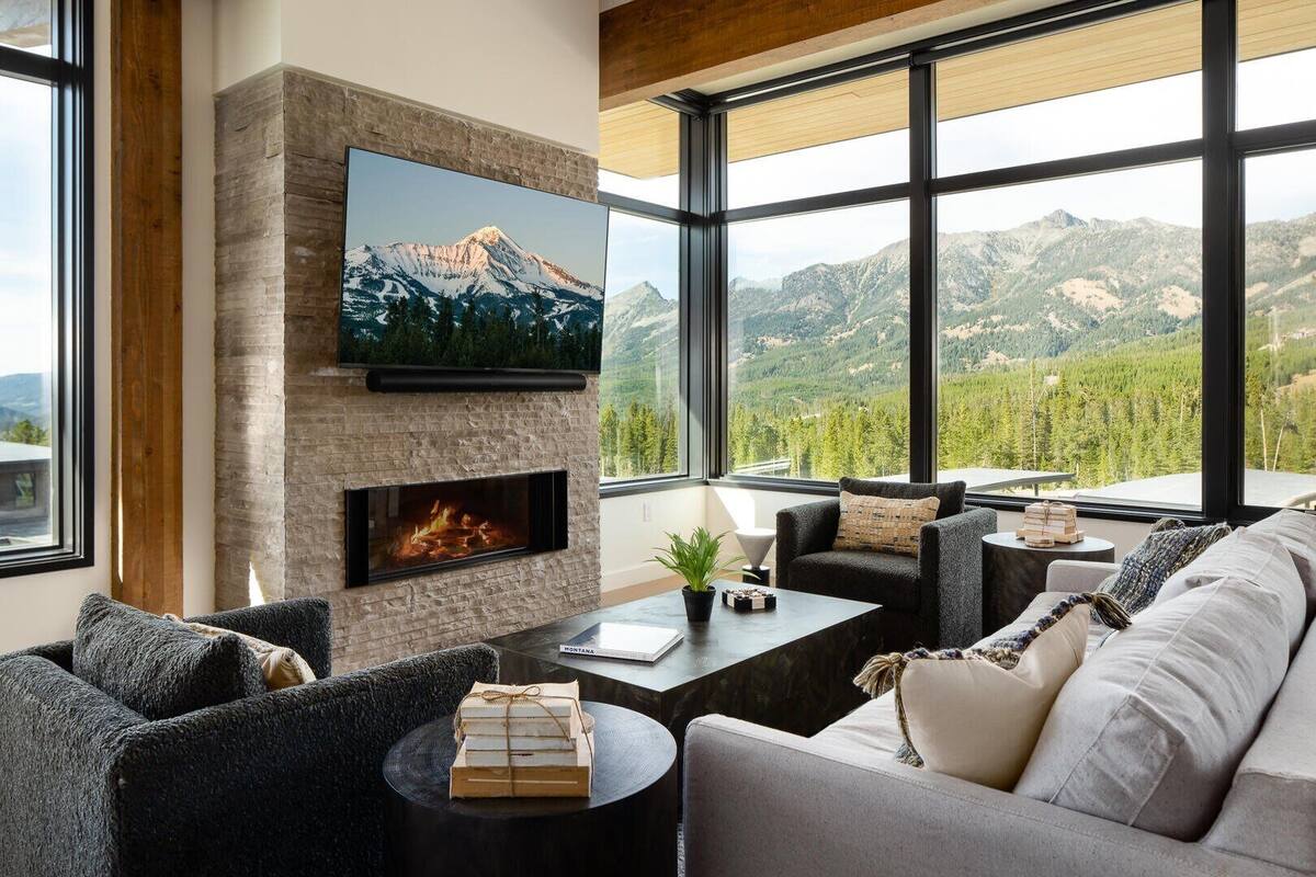 Ein modernes Wohnzimmer mit Kamin aus Stein, gemütlicher Sitzgelegenheit und einem großen Fenster mit Blick auf die Berge.