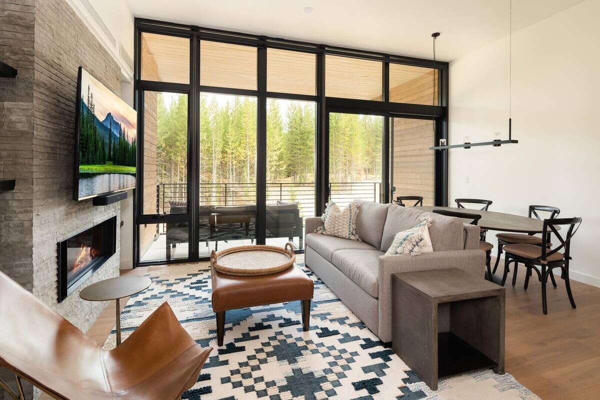 Ein modernes Wohnzimmer mit Kamin, großen Fenstern, einer Couch, einem Esstisch und einem an der Wand montierten Fernseher.