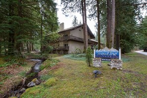 Eine Lodge namens SnowLine mit einem Steinschild, umgeben von dichtem Wald und einem kleinen Bach.