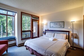 Ein Schlafzimmer mit einem großen Bett, einem Sessel, einer Stehlampe und einem Fenster mit Blick auf Bäume.