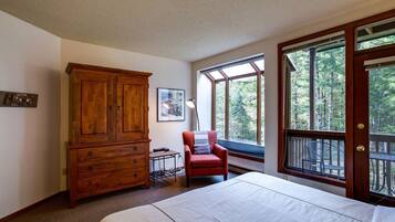 Un dormitorio con un armario de madera grande, una cama individual, un sillón rojo y una ventana con vistas a árboles.