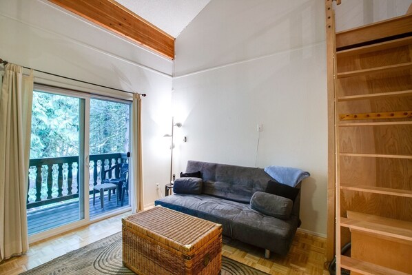 Ein Zimmer mit einer grauen Couch, einer Körbchentruhe und einer Holzleiter.