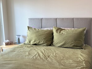 A bed with two pillows, a bedside table with a lamp and a tissue box, and a plain wall.