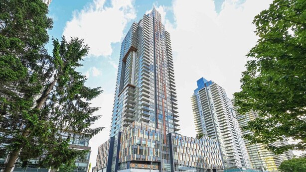 A modern high-rise building with a glass facade, surrounded by trees and other buildings. - Burnaby Metropolis Metrotown/1bedroom Condo/AC/Skytrain/Pool/Gym (Burnaby)