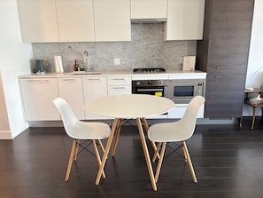 A modern kitchen with white cabinets, a gas stove, an oven, and a dining table with two chairs.