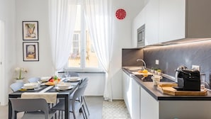 Eine moderne Küche mit integriertem Backofen und Spüle, eine Essecke mit Tisch für zwei Personen und ein Fenster mit transparenten Vorhängen.