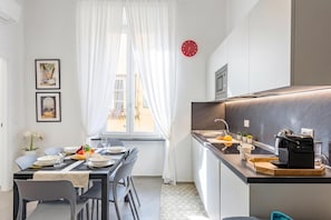 A modern kitchen with a built-in oven and a sink, a dining area with a table set for two, and a window with sheer curtains. - Lovely Apartment In Genova Historic Center A/C B, Genova, Italy (Genova)