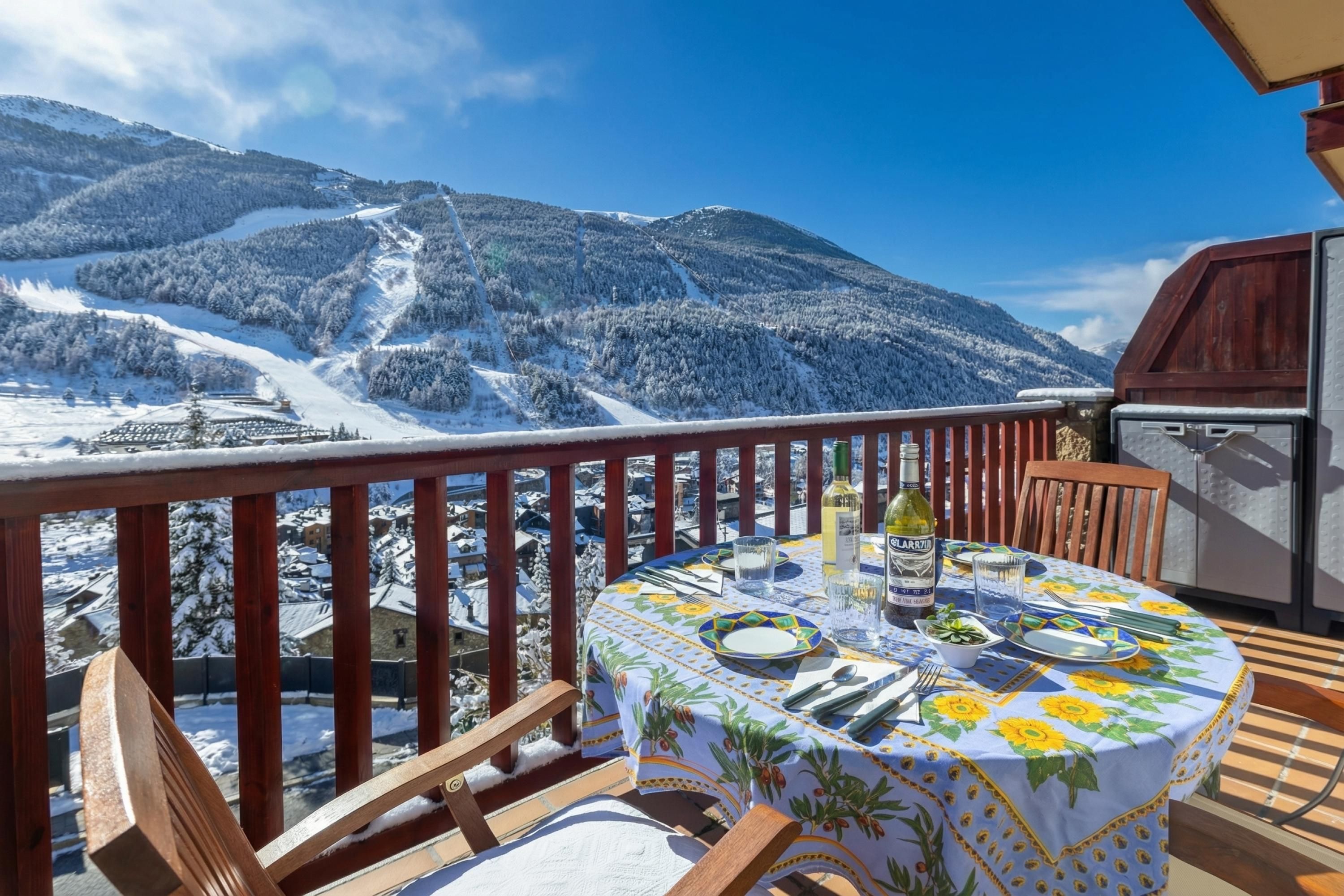 Un balcón con una mesa lista para comer, con vistas a un paisaje montañoso nevado.