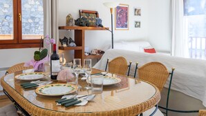 A dining area with a round glass table, wicker chairs, and a white bed in the background. - Andorra Stunning Views Apartment, El Tarter, Andorra (El Tarter)