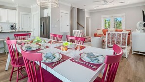 Eine moderne Küche mit weißen Schränken, einem Edelstahl-Kühlschrank und einem Essbereich mit einem weißen Tisch und rosa Stühlen.