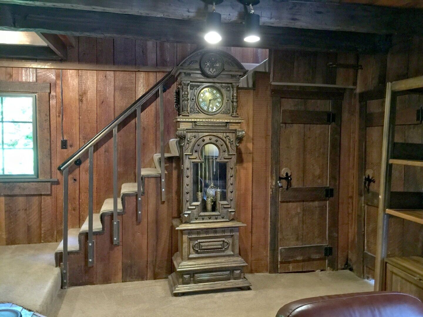 A room with wooden walls, a grand clock, a staircase, and a window.
