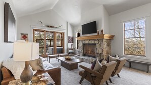 A spacious living room with a stone fireplace, comfortable seating, and large windows offering a view of the outdoors. - Park City Ski Resort - Town Pointe Condos (Park City)
