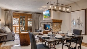 A cozy living room with a fireplace, a dining area with a table set for four, and a large window with curtains. - Park City Ski Resort - Town Pointe Condos (Park City)