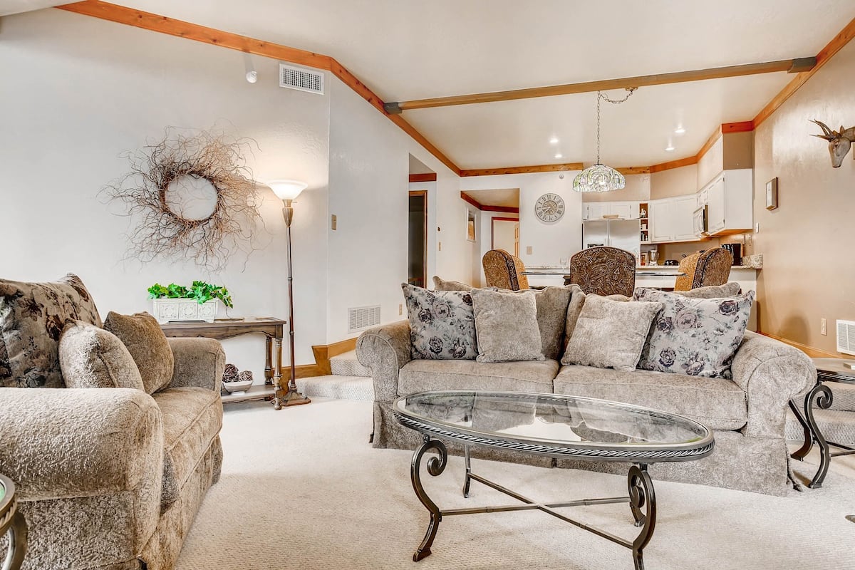 A cozy living room with a round glass coffee table, a sofa with patterned cushions, and a rustic wall decor.