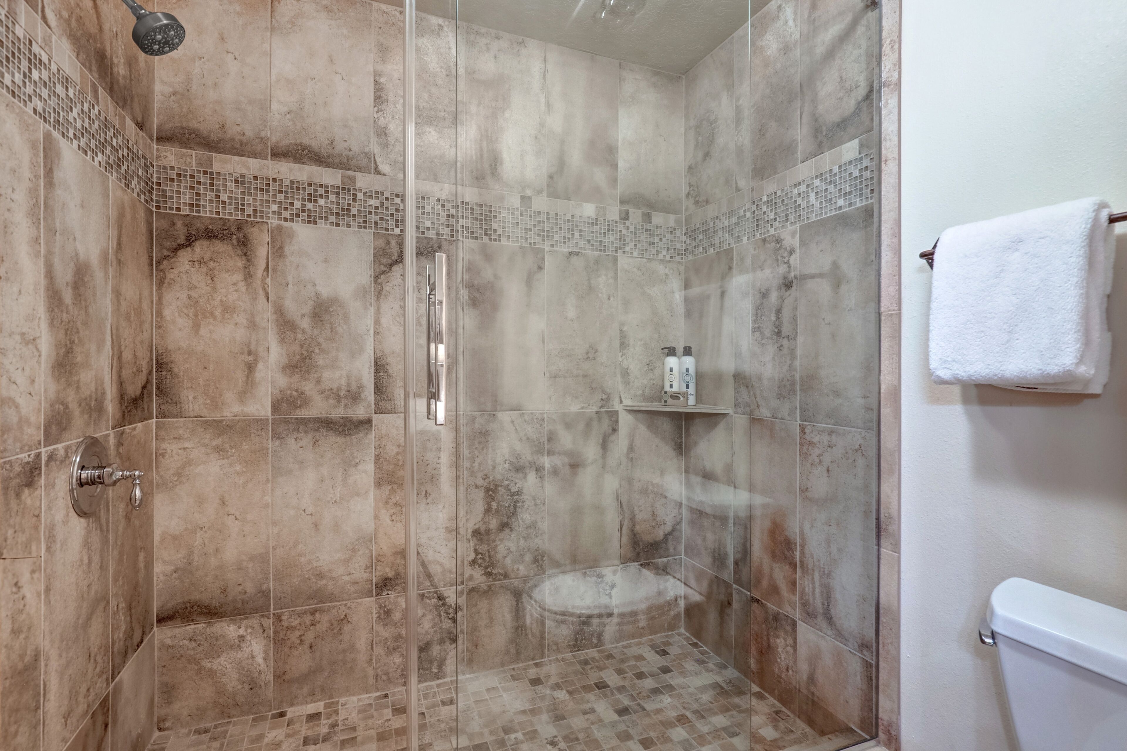 Eine Duschkabine mit Glaswänden, ein gefliestes Badezimmer mit Toilette in Weiß und ein weißes Handtuch an der Wand.