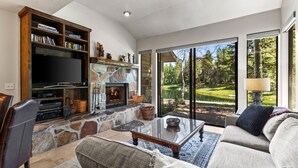 A living room with a stone fireplace, a television, and a view of a golf course.