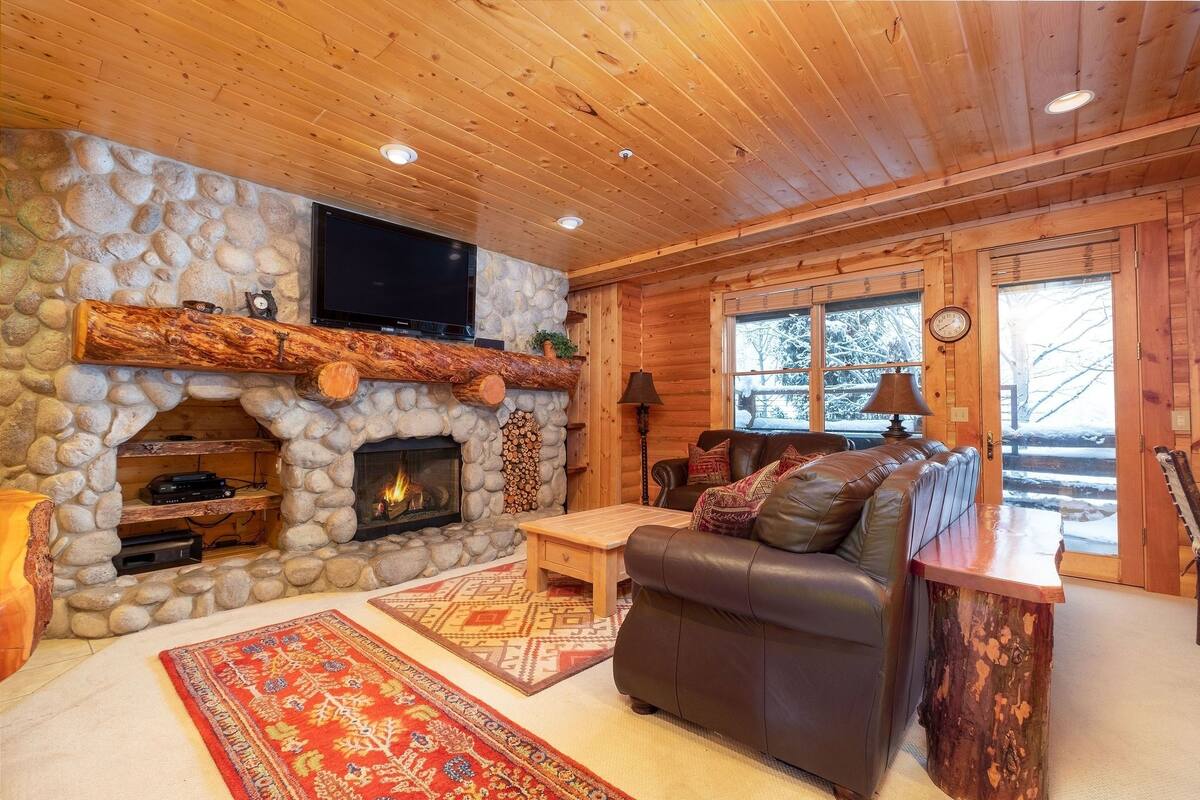 A cozy cabin interior with a stone fireplace, leather sofa, and a television mounted above it.