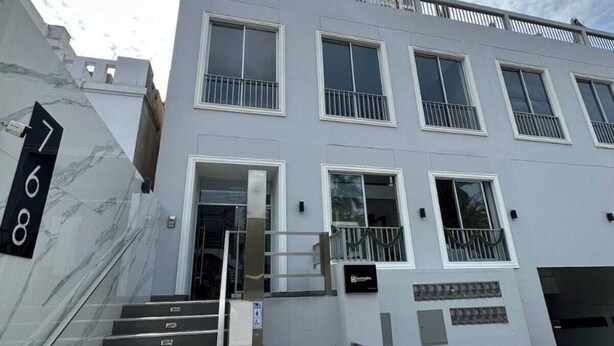 A modern building with a staircase leading to a door, a fire hydrant, and bollards on the sidewalk. - Apartment in front of Parque de las Aguas (Lima)