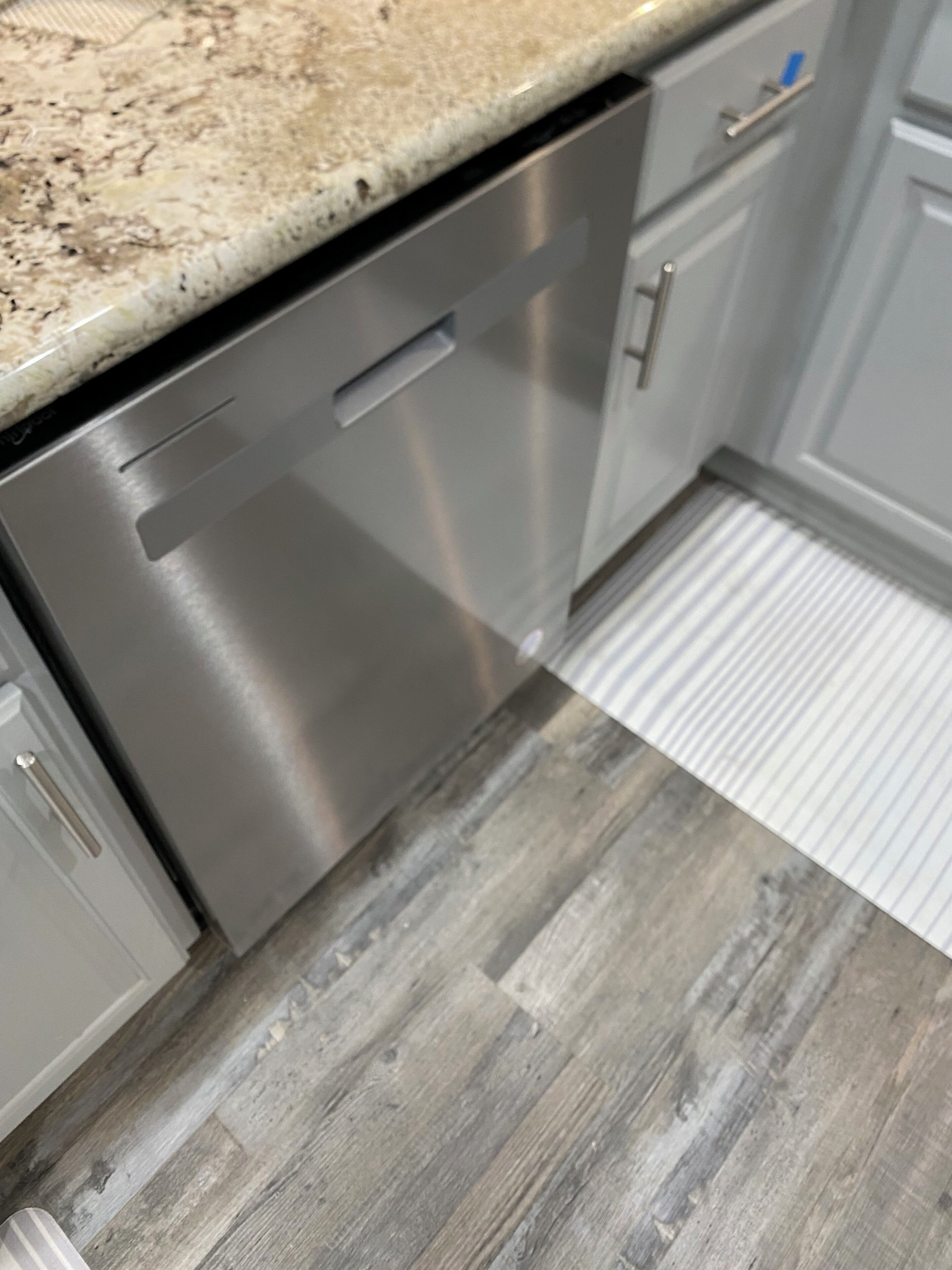 A kitchen with a stainless steel dishwasher, grey cabinets, and a wooden floor.