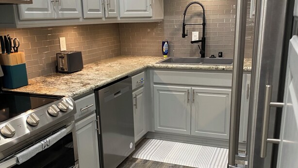 Una cocina moderna con armarios blancos, un refrigerador de acero inoxidable, horno empotrado, lavavajillas y encimera de granito.