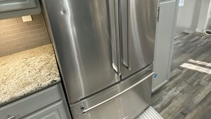 Un refrigerador de acero inoxidable en una cocina con gabinetes grises y una encimera de granito.