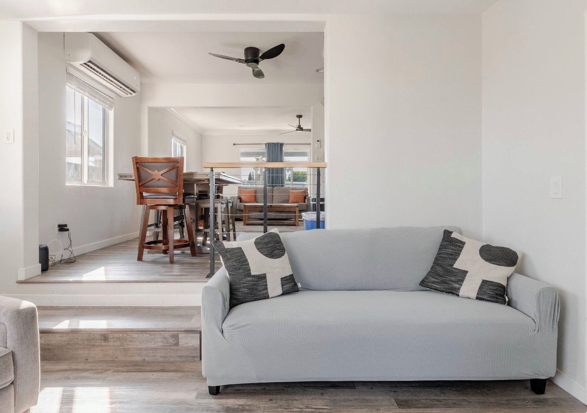 A modern living room with a grey sofa, a wooden chair, and a dining area in the background.