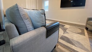 Una sala de estar con un sofá gris, un mueble multimedia negro, un televisor grande en la pared y una alfombra estampada.