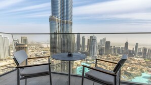 Un balcone con due sedie e un tavolo, affaccia su una città con edifici alti e un'area d'acqua.