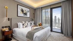 Una camera d'albergo moderna con un letto grande, un comodino, un tavolino di fianco al letto, un'opera d'arte incorniciata, una finestra con tende e vista sulla città.