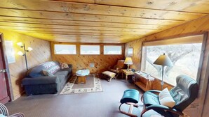 Interior acogedor de una cabaña con sofá, sillón y una mesita con lámpara.