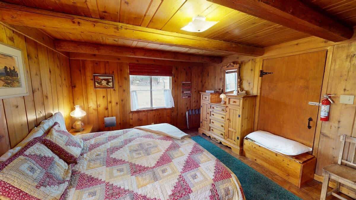 Ein Zimmer in einer Holzhütte mit einem Bett, einem Schminktisch und einem Fenster.