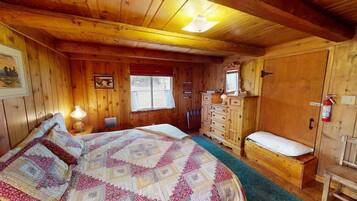 Ein Zimmer in einer Holzhütte mit einem Bett, einem Schminktisch und einem Fenster.