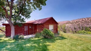 Una cabaña de troncos con fachada roja, una puerta principal y un porche pequeño.