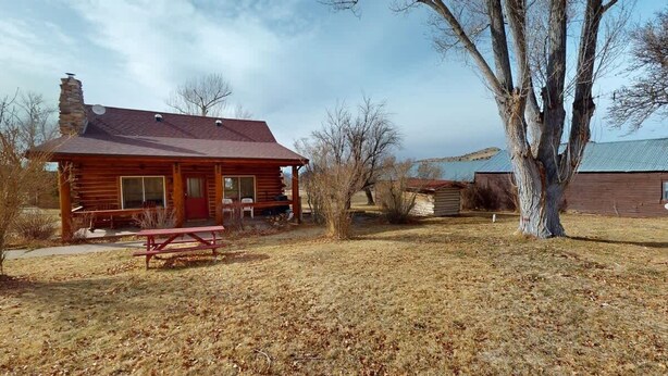 A rustic log cabin with a red door, a picnic table, and a large tree in the foreground. - Pack Creek - M4, Log Cabin at Pack Creek Ranch (Moab)
