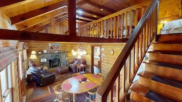 A wooden cabin interior with a dining area, a fireplace, and a staircase.