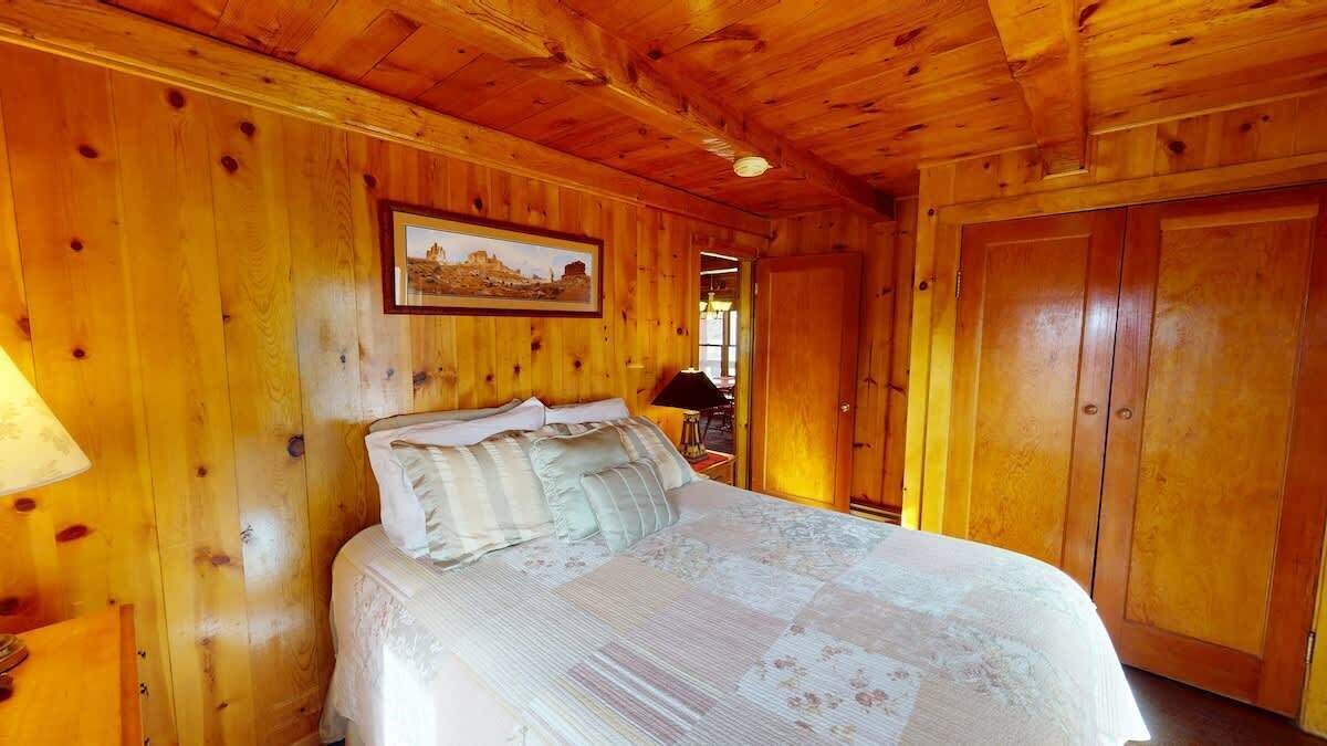 Ein Zimmer mit Holzwänden, einem Bett, einem gerahmten Bild an der Wand und einer Tür.