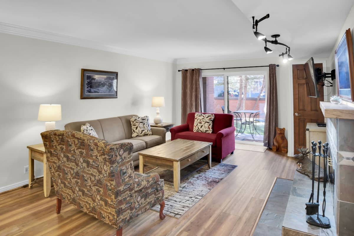 Een woonkamer met een gestreept fauteuil, een rode bank, een houten salontafel en een open haard met een beerbeeld.