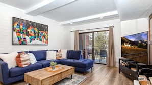 Un salon moderne avec un canapé d’angle bleu, une table basse en bois et un grand tableau accroché au mur.