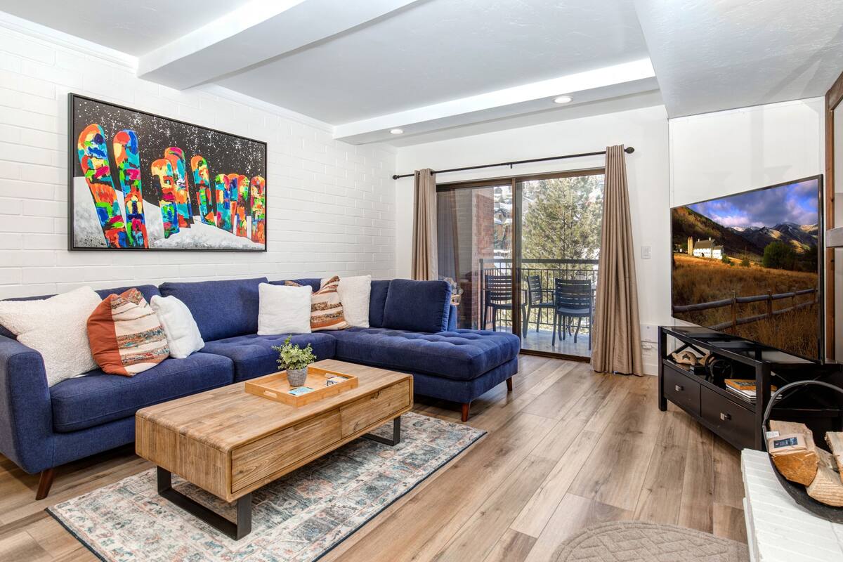 Een moderne woonkamer met een blauwe modulaire bank, een houten salontafel en een groot schilderij aan de wand.