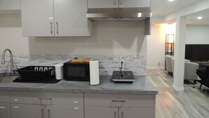 A modern kitchen with grey cabinets, a stainless steel range hood, and a countertop with a microwave, toaster, and a black basket. - Cozy 2-Bedroom basement Suite with Private entrance South Winnipeg. (Winnipeg)