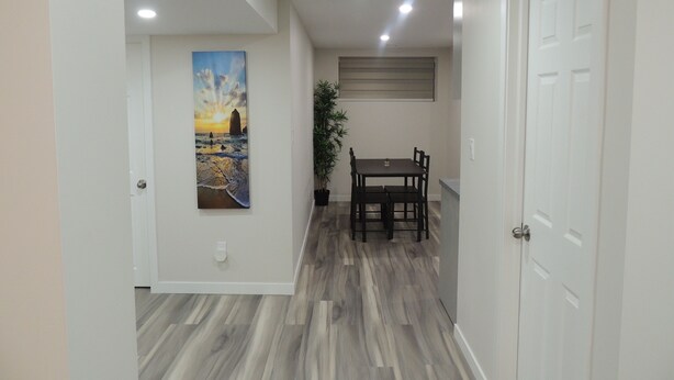 A hallway with a dining area featuring a table and chairs, a potted plant, and a painting of a sunset over the ocean. - Cozy 2-Bedroom basement Suite with Private entrance South Winnipeg. (Winnipeg)