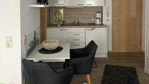Une cuisine compacte avec des meubles blancs, une machine à café et un coin repas comprenant deux chaises et une table.