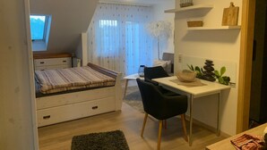 Une chambre à coucher comprenant un lit, un bureau, une chaise, une petite table et une fenêtre avec des rideaux.