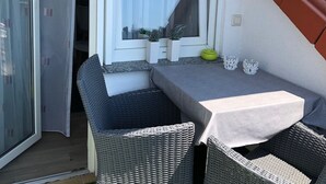 Une pièce d’angle avec une table et deux chaises en osier, une fenêtre avec un rideau et une petite plante en pot.