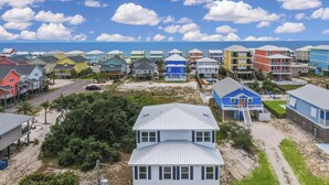 A coastal residential area with colorful houses, a prominent white house in the foreground, and a beach in the background.